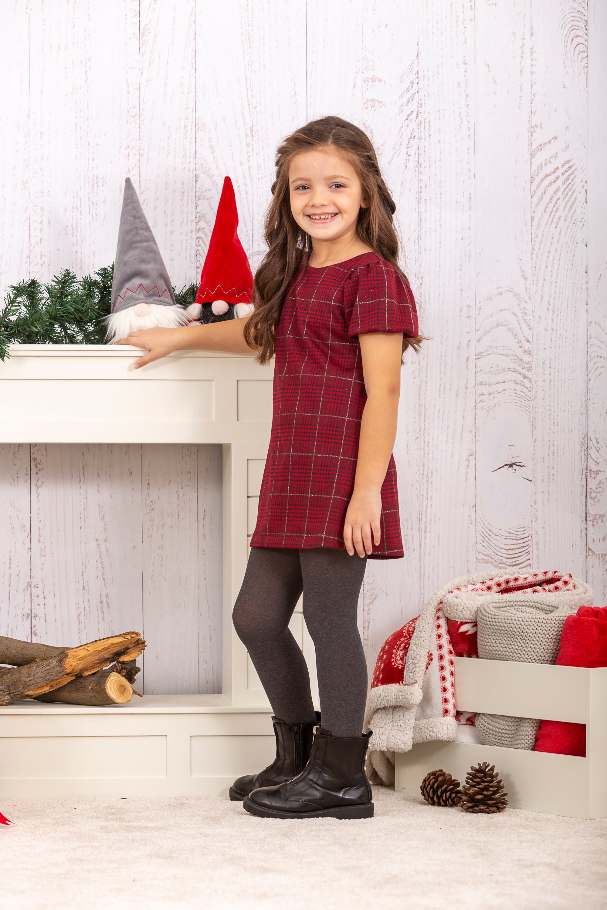 Niña de pie con vestido cuadros rojo de manga corta, look invierno junto a decoración Charanga